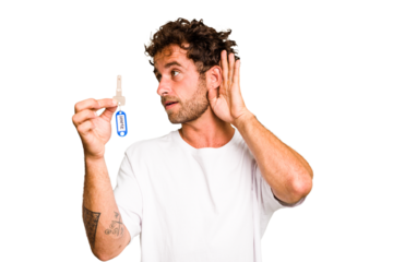 Young caucasian man holding home keys isolated trying to listening a gossip.