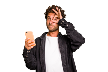 Young caucasian man using mobile phone isolated excited keeping ok gesture on eye.