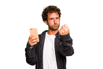 Young caucasian man using mobile phone isolated showing fist to camera, aggressive facial expression.