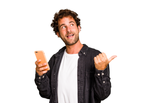 Young caucasian man using mobile phone isolated points with thumb finger away, laughing and carefree.