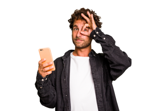 Young caucasian man using mobile phone isolated excited keeping ok gesture on eye.