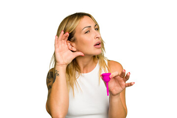 Fototapeta premium Young caucasian woman holding menstrual cup isolated on green chroma background trying to listening a gossip.