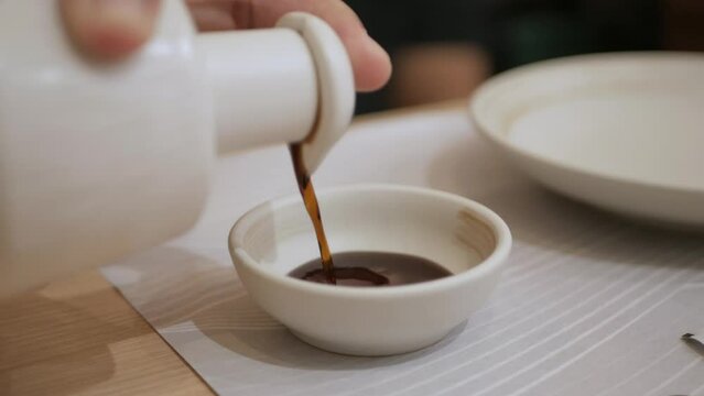 close up shot while pouring soy sauce into sauce plate for sashimi sushi japanese food meal. Asian food