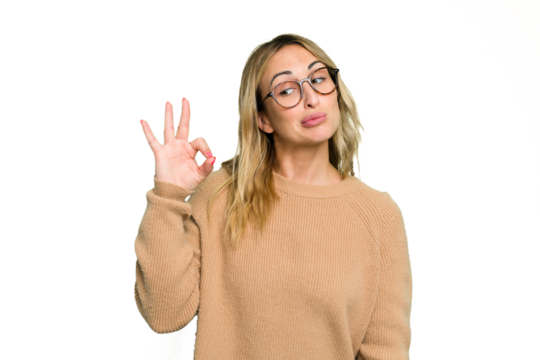Young caucasian woman isolated on green chroma background winks an eye and holds an okay gesture with hand.