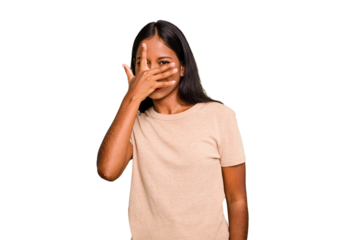Young Indian woman isolated blink at the camera through fingers, embarrassed covering face.