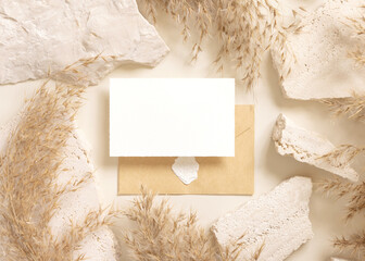 Card and enveelope near beige travertine stones and dried pampas grass top view, mockup
