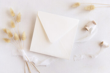 Square envelope near silk ribbons and dried hare's tail grass top view on white, boho mockup
