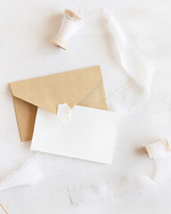 Fototapeta premium Card and envelope near silk ribbons top view on white, romantic wedding mockup