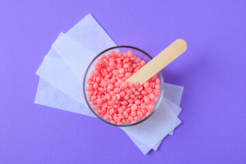 Pink granules of wax for depilation in a glass bowl and depilatory strips on a lilac background. Epilation, depilation, waxing, unwanted hair removal procedure. - obrazy, fototapety, plakaty