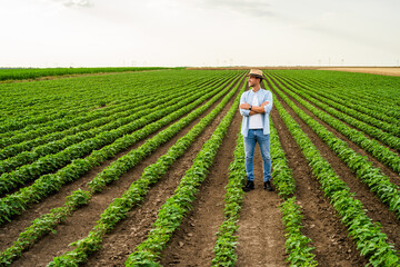 Happy farmer is standing in his growing soybean field.	