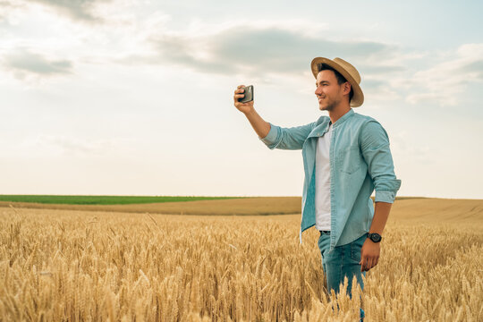 Happy farmer photographing crops with phone while standing in his growing wheat field.	