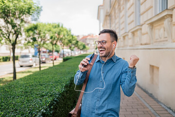Enthusiastic young adult entrepreneur business man, listening to music, singing and dancing outside.