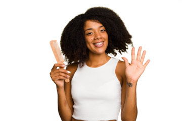 Young african american woman holding hair comb isolated smiling cheerful showing number five with fingers.