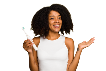 Young african american woman holding an electric toothbrush isolated showing a copy space on a palm and holding another hand on waist.