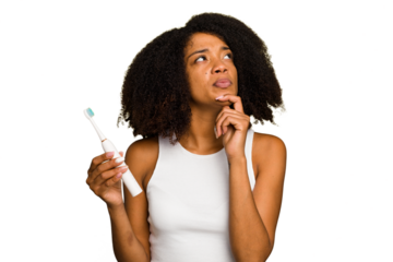 Young african american woman holding an electric toothbrush isolated looking sideways with doubtful and skeptical expression.