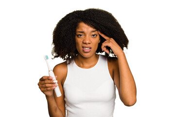 Young african american woman holding an electric toothbrush isolated showing a disappointment gesture with forefinger.