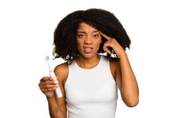 Young african american woman holding an electric toothbrush isolated showing a disappointment gesture with forefinger.