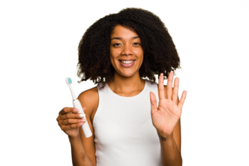 Young african american woman holding an electric toothbrush isolated smiling cheerful showing number five with fingers.