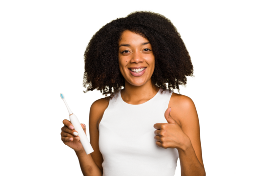 Young african american woman holding an electric toothbrush isolated smiling and raising thumb up
