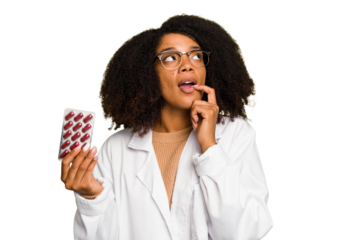 Young pharmacist African American woman holding a tablet of pills isolated relaxed thinking about something looking at a copy space.