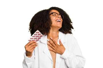 Young pharmacist African American woman holding a tablet of pills isolated laughs out loudly...