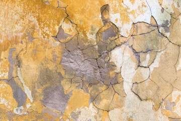 Cracked, broken concrete texture on a rough, patched, yellow wall. Close up background design element.