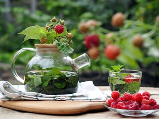 Autumn warming medicinal tea with raspberry and mint in a glass cup and teapot on a natural background.
