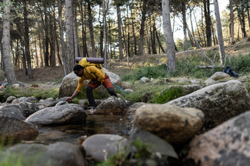 hiker man happy in the nature, take water from the river to drink, African man adventurous traveler,