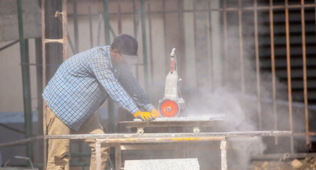 A worker wearing gloves uses an angle grinder to cut porcelain stoneware tiles, highly skilled...