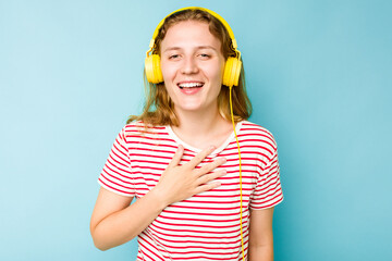 Young caucasian woman wearing headphones isolated on blue background laughs out loudly keeping hand on chest.