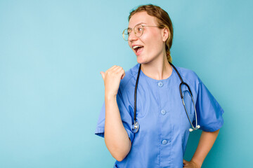 Young nurse caucasian woman isolated on blue background points with thumb finger away, laughing and carefree.