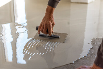 Grey self-leveling screed, new floor layer, man hand.