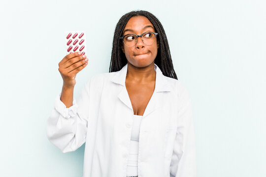 Young African American pharmacist woman isolated on blue background confused, feels doubtful and unsure.