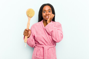 Young African American woman holding a bathtub brush isolated on blue background biting fingernails, nervous and very anxious.