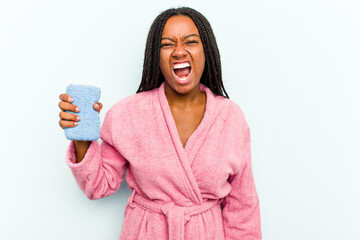 Young African American woman holding a sponge isolated on blue background  screaming very angry and...
