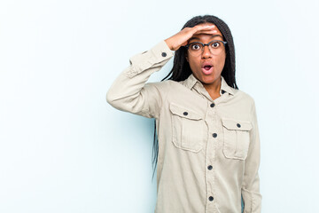 Young African American woman with braids hair isolated on blue background looking far away keeping hand on forehead.