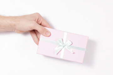 male hand holding a pink box with a bow on a white