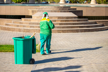 The janitor cleans the city street with a broom in the city. Street cleaning service. A worker sweeps the sidewalks in the park with a vine.