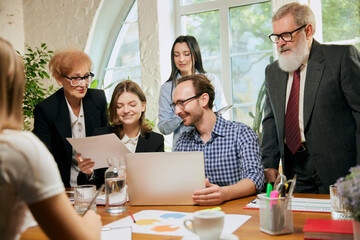 Friendly atmosphere at business gathering. Mixed ages people talking, working with colleagues at loft style office space, indoors.