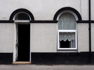 open front door and window of a typical old brick british terraced house with black and white decorative paintwork