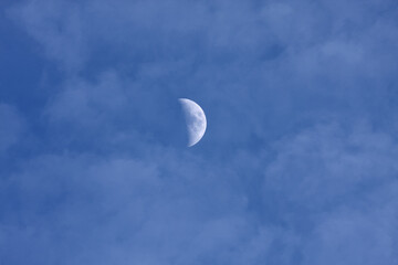 half moon in late afternoon cloudy blue sky