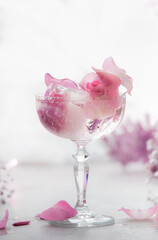 Fancy drink in wide champagne glass with pink flowers and ice cubes