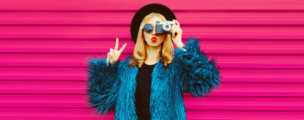 Portrait of stylish blonde young woman photographer with film camera taking picture and blowing her...