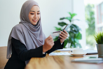 Beautiful Muslim woman shopping online using her phone and credit card