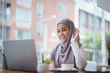 Beautiful Muslim woman using computer to greet attendees via video conference