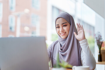 Beautiful Muslim woman using computer to greet attendees via video conference