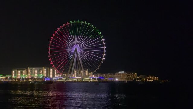 Night view of Bluewater artificial island with one of the largest Ferris wheel in the world 'Ain Dubai' lit up like the UAE flag at JBR Beach