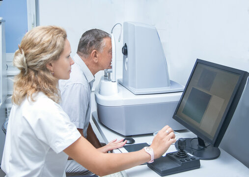 an elderly man on a CT scanner does a retinal tomography in the oculist's office. brain, a female optometrist is sitting at a computer..
