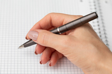 Elegant female hand with a pen over a white sheet of paper. The woman writes with a pen. Premium pen in a female hand. Elegant female hand with perfect manicure. Symbol of business and office work. 