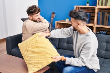 Young couple fighting with cushion sitting on sofa at home